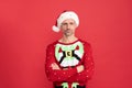Serious man in Santa Claus hat and Christmas jumper stand keeping arms crossed, new year