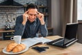 Serious man sit at table in kitchen and reading. He look down at journal and hold hands on head. Man look concentrated.