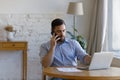 Serious man use laptop, talks on cellphone seated at workplace Royalty Free Stock Photo