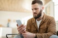 Serious Man Using Smartphone Wearing Earbuds Earphones At Home