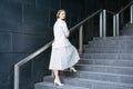 Serious mature businesswoman in elegant dress standing on stairs in front