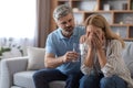 Serious mature caucasian husband calm upset crying wife, gives glass of water, lady suffers from pain and depression