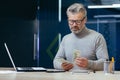 Serious mature investor working inside office, senior gray haired businessman counting money cash