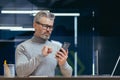 Serious mature man inside office using app on phone, senior gray haired businessman reading thinking message sitting at Royalty Free Stock Photo