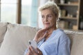 Serious mature senior woman lady holding mobile phone on couch Royalty Free Stock Photo