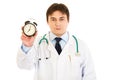 Serious medical doctor holding alarm clock in hand