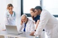 Serious medical team of multiethnic doctors talking together concentrated looking to laptop screen standing on Royalty Free Stock Photo