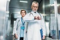 serious middle aged male doctor checking wristwatch while his female colleague standing behind in hospital Royalty Free Stock Photo