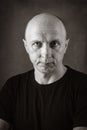 A serious middle-aged man with an unshaven face and a bald head, looking directly into the camera. Black and white portrait toned Royalty Free Stock Photo