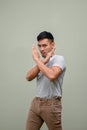 Serious Asian man with crossing hands gesture stands against a green studio background