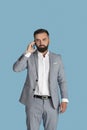 Serious millennial businessman in office wear having conversation on smartphone on blue studio background Royalty Free Stock Photo