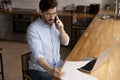 Millennial male working by laptop holding letter making phone call