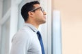 Serious mixed race businessman looking out of a window standing alone in an office at work. One hispanic standing and Royalty Free Stock Photo