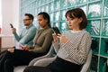 Serious multicultural young business people sitting in row using smartphones, waiting for job interview, sitting in Royalty Free Stock Photo