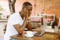 Serious multiracial businessman using laptop in cafe with head in hands in cafe. Video call and read finance information Royalty Free Stock Photo