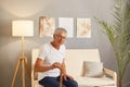 Serious old disabled man holding hands on wooden stick, resting on cozy couch in living room elderly senior grandfather wearing Royalty Free Stock Photo