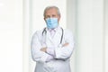 Serious old doctor with medical mask and folded arms. Royalty Free Stock Photo