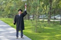 A serious old man in a graduate robe pulls his hand with a diploma up outdoors.