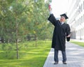 A serious old man in a graduate robe pulls his hand with a diploma up outdoors.