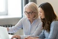 Serious old mentor teaching intern or student pointing at laptop