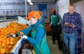 Serious owner of fruit warehouse checking work of female employees engaged in tangerines sorting
