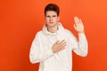 Serious patriotic male in white sweatshirt with hood holding hand on heart, juryman swearing to speak truth in court, honor and
