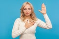 Serious patriotic woman with curly blond hair raising one arm and putting on chest another making oath, swearing