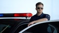 Serious patrolman in sunglasses monitoring road standing near door of police car Royalty Free Stock Photo