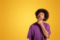 Serious pensive black adult curly man in purple t-shirt, thinks, look at copy space