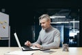 Serious and pensive mature investor working inside modern office, senior gray-haired businessman using laptop at work Royalty Free Stock Photo