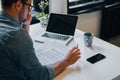 Serious pensive thoughtful focused young casual businessman or entrepreneur in office filling income tax return papers documents