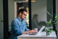 Serious pensive thoughtful focused young casual businessman or entrepreneur in office looking at and working with laptop making