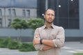 Serious and pensive young office worker with crossed arms looking at camera, businessman in shirt outside office Royalty Free Stock Photo