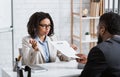 Serious personnel manager taking resume from young job applicant on work interview at modern company office