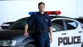Serious policeman in uniform leaning on patrol car, maintenance of order, duty Royalty Free Stock Photo