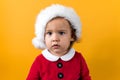 Serious Portraite Cute Happy Cheerful Chubby Baby Girl in Santa Hat Looking On Camera At Yellow Background. Child Play