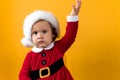 Serious Portraite Cute Happy Cheerful Chubby Baby Girl in Santa Hat Waving Hand Up At Yellow Background. Child Play Royalty Free Stock Photo