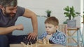Serious preschool child is playing chess with his parent thinking about next move and moving chesspieces while his