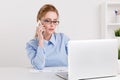 Serious pretty blonde woman working at office by her nboteboo and talking her phone. Royalty Free Stock Photo