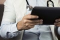 Serious professional doctor in white coat and stethoscope holding modern touch screen gadget using digital tablet computer at work Royalty Free Stock Photo