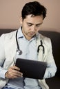 Serious professional doctor in white coat and stethoscope holding modern touch screen gadget using digital tablet computer at work Royalty Free Stock Photo