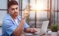A focused young experienced male doctor in a blue uniform sits at a table and consults a patient. Royalty Free Stock Photo