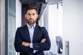 A serious and proud young man businessman walks in a business suit in the hall of an office building, crosses his arms Royalty Free Stock Photo