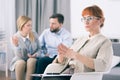 Serious psychologist making a hand gesture while a married couple is talking in the background