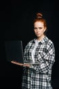 Serious sad young woman holding laptop computer and looking at camera on isolated black background. Royalty Free Stock Photo