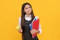 Serious school-aged girl child think holding apple and books yellow background, thinking