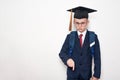 Serious schoolboy in a suit, glasses and an academic hat is pointing down. School concept. White background