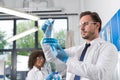 Serious Scientist Looking At Flask With Blue Liquid In Laboratory Over Group Of Scientific Researchers Making Royalty Free Stock Photo