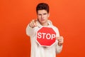 Serious self confident teenager in casual white sweatshirt with hood pointing finger on you holding stop sign, warning to adhere Royalty Free Stock Photo