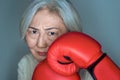 senior asian woman standing in a fighting pose with red boxing gloves on blue background. Feminism, women power concept